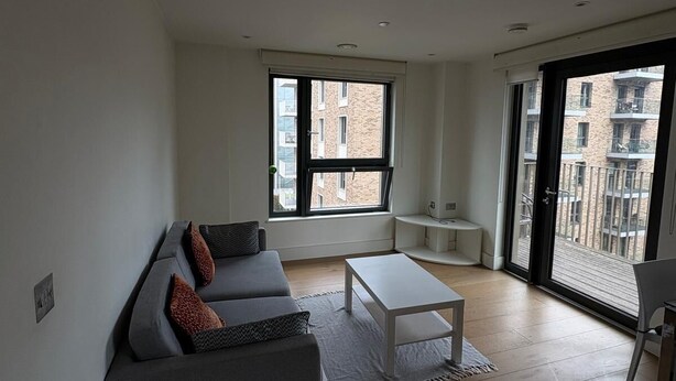 Een moderne woonkamer met een grijze bank, een witte salontafel en een groot raam met uitzicht op gebouwen.