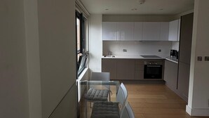 Een moderne keuken met witte kasten, een inbouwoven en een eethoek met een glazen tafel en twee stoelen.