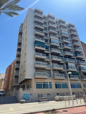 A multi-story residential building with balconies, a staircase leading to the entrance, and a graffiti-covered wall. - Apartment on the beach - Paseo marítimo de Almería (Almería)