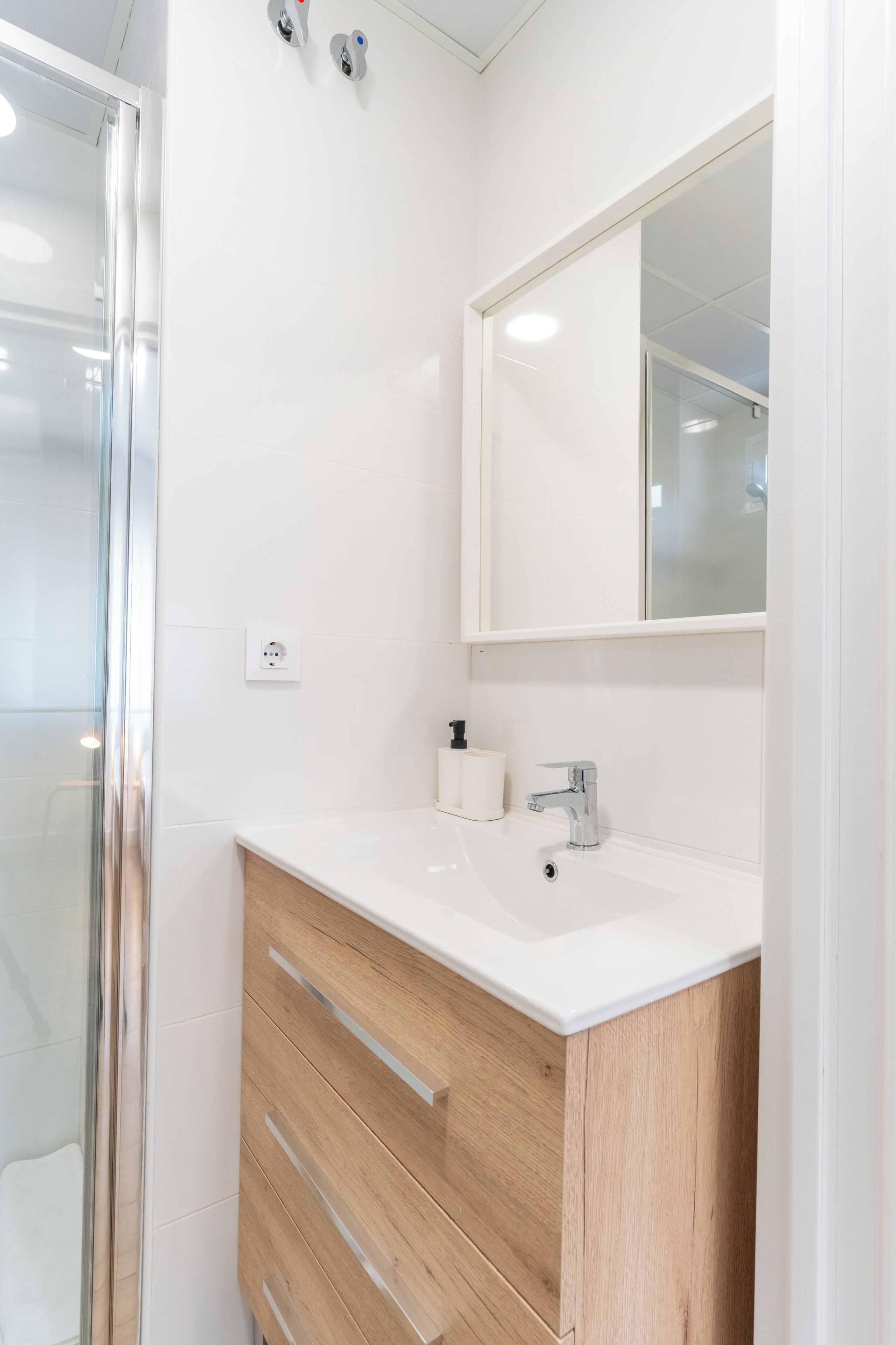 Ein modernes Badezimmer mit Duschkabine aus Glas, einem weißen Waschbecken, einem Spiegel und Holzschränken.
