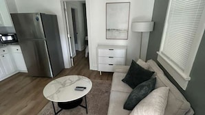 Ett kompakt vardagsrum med en soffa, ett soffbord, ett kylskåp, en mikrovågsugn och en mönstrad matta.