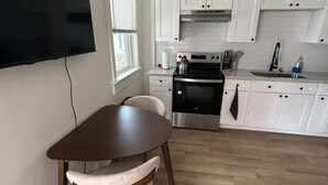 Ett modernt kök med vita skåp, en platt-TV som är monterad på väggen, ett matbord med stolar och ett trägolv.