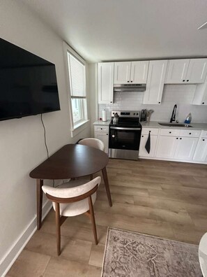 Eine moderne Küche mit weißen Schränken, einem flachbildfernseher an der Wand, einem Esstisch mit Stühlen und Holzboden.