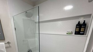 Ett badrum med en dusch som är avskärmad med glasväggar, en vit toalett och ett vitt badkar.