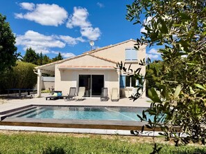 Ein Haus mit Swimmingpool, Sitzgelegenheiten im Freien und einer überdachten Terrasse.