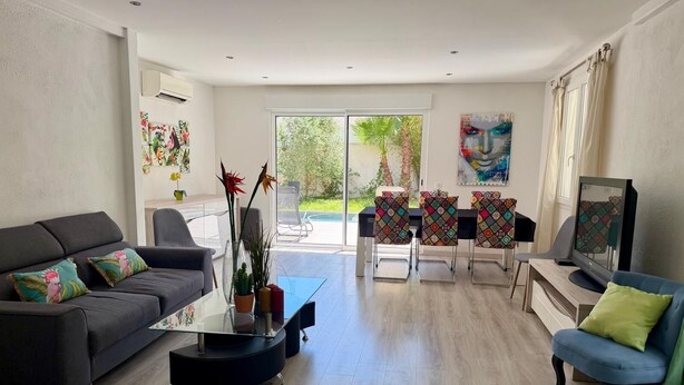 A modern living room with a sofa, coffee table, TV, and a dining area with chairs and a table. - Villa Saphir - Elegant family villa for 10 people with private pool in Occitanie, France (Saint-Jean-de-Cornies)