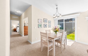 A dining area with a table, chairs, and a vase of flowers. There is a hallway leading to another room with a bed and dresser.