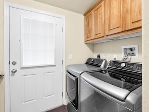 A laundry room with a white door, wooden cabinets, a stainless steel washer and dryer, and a water heater.