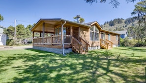 A wooden cabin with a porch, a staircase, and a stone foundation.