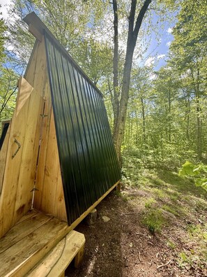 Une structure en bois dotée d’un toit incliné, entourée d’une zone boisée.