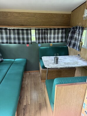Ein kompaktes Wohnmobil-Interieur mit Essbereich, zwei Sitzgruppen und Karomustert-Vorhängen.