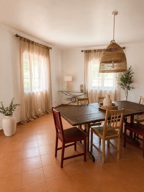 A dining area with a wooden table, chairs, a hanging light fixture, and a potted plant.