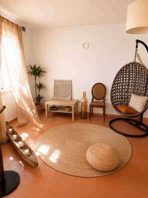 A living room with a hanging chair, a round woven rug, a wooden table, and a potted plant.