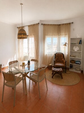 A dining area with a glass table, wicker chairs, a leather armchair, and a bookshelf.