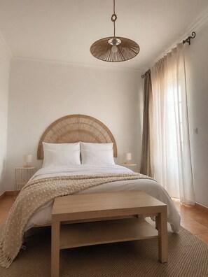 A bedroom with a wooden bed, a woven headboard, a hanging light fixture, and sheer curtains.