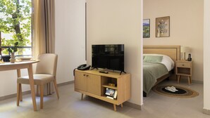 Habitación de hotel con una cama, un televisor sobre un mueble de madera, un escritorio con una silla y una ventana con cortinas.