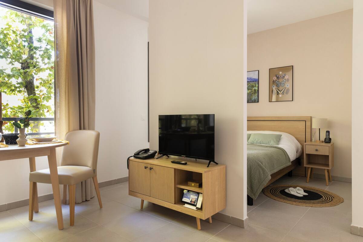 Habitación de hotel con una cama, un televisor sobre un mueble de madera, un escritorio con una silla y una ventana con cortinas.