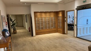 Un hall de hotel con un mostrador de recepción de madera, una planta en maceta, un extintor y un panel de seguridad fijado a la pared.