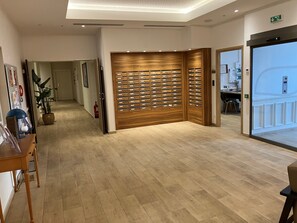 Un hall d’hôtel avec un comptoir d’accueil en bois, une plante en pot, un extincteur et un panneau de sécurité fixé au mur.