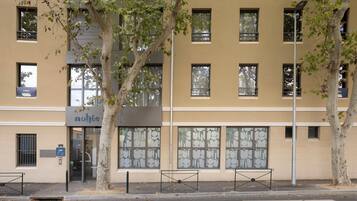 Un bâtiment avec de nombreuses fenêtres, un arbre devant et un banc sur le trottoir.