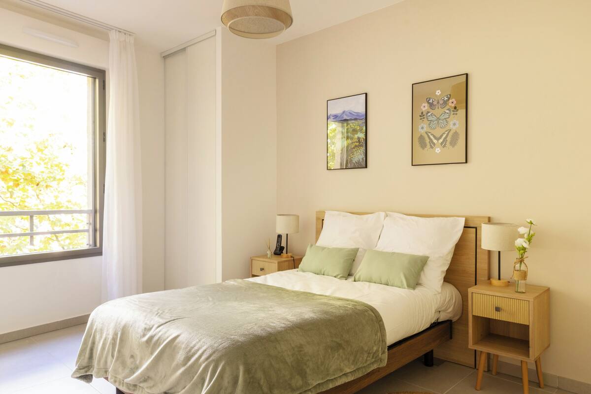 Un dormitorio con cama, mesitas de noche, una ventana y dos obras de arte colgadas en la pared.