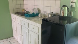 A kitchen with white cabinets, a black refrigerator, a kettle, and a green dish rack. - The Victor's Inn  (Gros Islet)