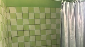A bathroom with green and white tiled walls, a shower curtain, and a tiled floor. - The Victor's Inn  (Gros Islet)