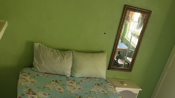 A bed with floral bedding, a white pillow, a folded towel, and a remote control on a nightstand. - The Victor's Inn  (Gros Islet)