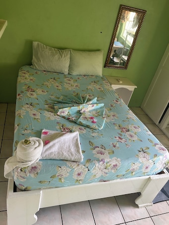 A bed with floral bedding, a white pillow, a folded towel, and a remote control on a nightstand.