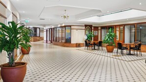 A spacious hotel lobby with a patterned floor, large potted plants, a chandelier, and a seating area with tables and chairs. - Glebe Corner Walkable City Fringe Base with Pool (Glebe)