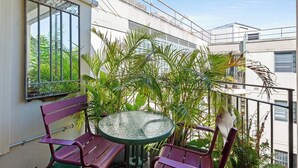 A balcony with a round table and two chairs, surrounded by lush green plants. - Glebe Corner Walkable City Fringe Base with Pool (Glebe)