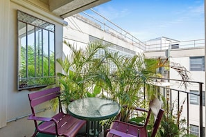 Ein Balkon mit rundem Tisch und zwei Stühlen, umgeben von üppigem Grün.