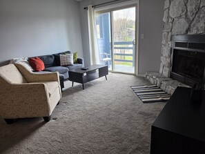 Ein Wohnzimmer mit einer Couch, einem Couchtisch, einem Kamin und Blick durch eine Glastür.