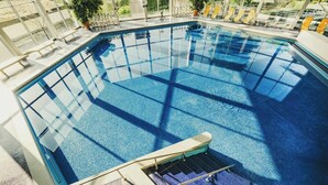 Ein Hallenbad mit großen Glaswänden, hellem Innenraum und einer Liegebereich mit Liegestühlen.