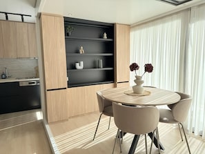A modern kitchen with wooden cabinets, a built-in black shelf unit, and a dining area with a round table and chairs.