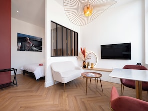 Een moderne woonkamer met een bank, een eettafel, een televisie en een bijzondere plafondlamp.