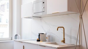 Una cocina moderna con encimera blanca, grifo dorado, microondas y cafetera.