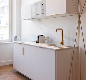 Una cocina moderna con encimera blanca, grifo dorado, microondas y cafetera.