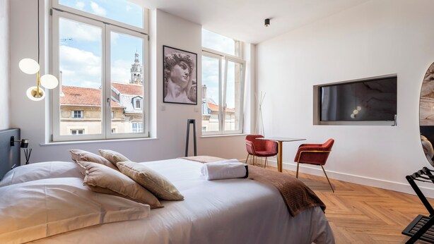 A modern bedroom with a large bed, two red chairs, a TV, and large windows with a city view. - Les perchoirs de Stanislas 2 - logement de standing hyper centre (Nancy)