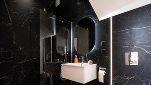 A modern bathroom with a white sink, mirror, and toilet, set against dark marble walls. - Les perchoirs de Stanislas 2 - logement de standing hyper centre (Nancy)