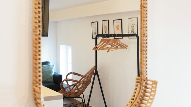 A room with a mirror, a wicker chair, a black hanger stand, and a wall-mounted picture frame. - Le 302 Sainte Ségolène (Metz)