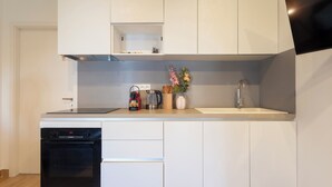 A modern kitchen with white cabinetry, a built-in oven, a coffee maker, and a sink. - Le 302 Sainte Ségolène (Metz)