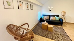 A living room with a black sofa, a woven chair, a patterned rug, and wall-mounted artwork. - Le 302 Sainte Ségolène (Metz)