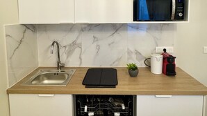 Ett kompakt kök med inbyggd diskmaskin, diskho, mikrovågsugn och kaffebryggare.