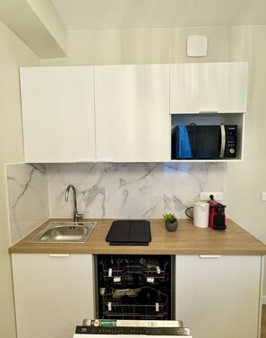 Una cocina compacta con lavavajillas integrado, un fregadero, microondas y cafetera.