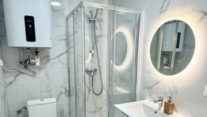 Ett modernt badrum med en duschavdelning med glasväggar, en toalett, ett handfat med spegel och en handdukshängare.