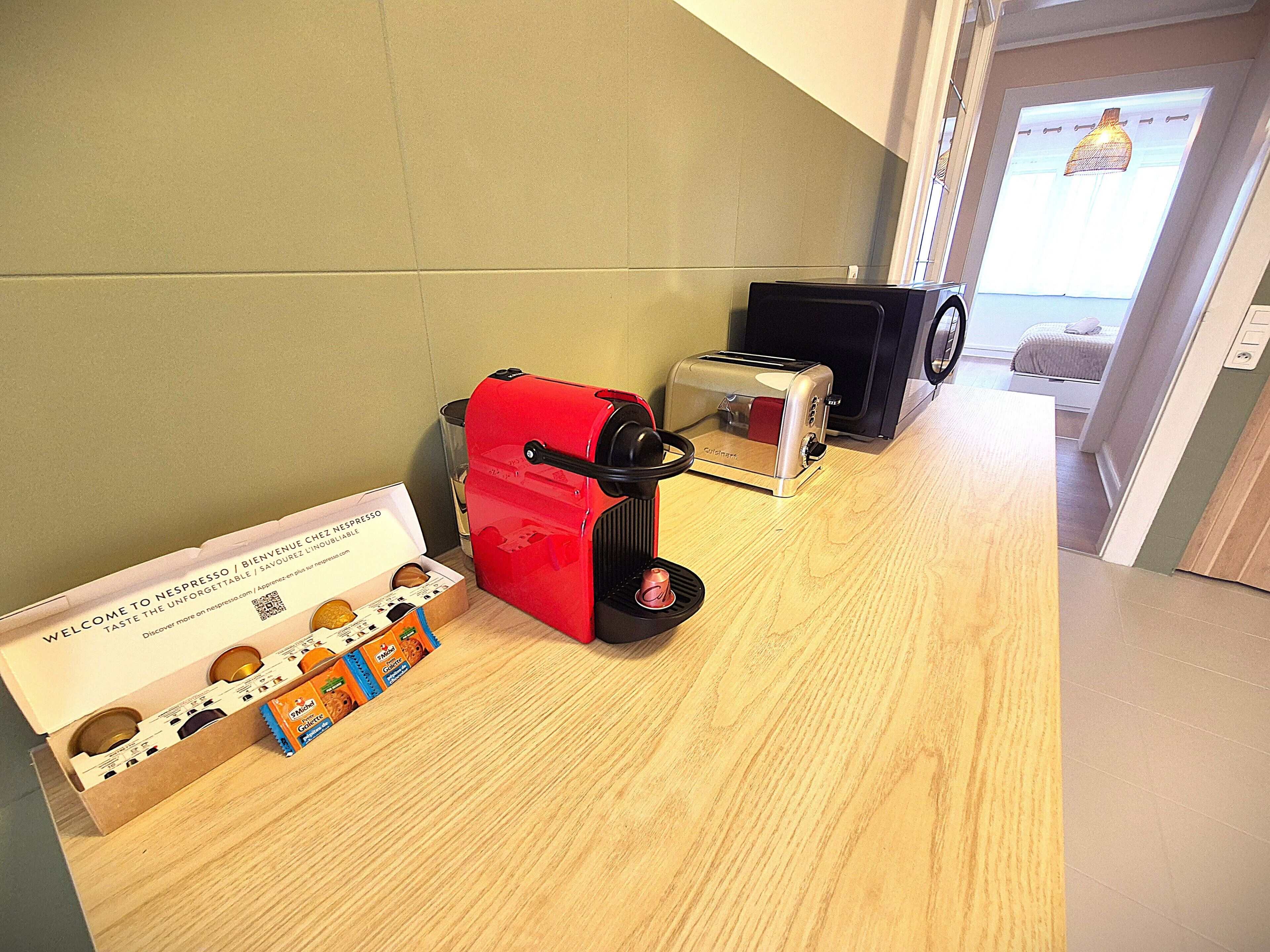 Una kitchenette con una cafetera roja, un tostador y una caja de cápsulas Nespresso.