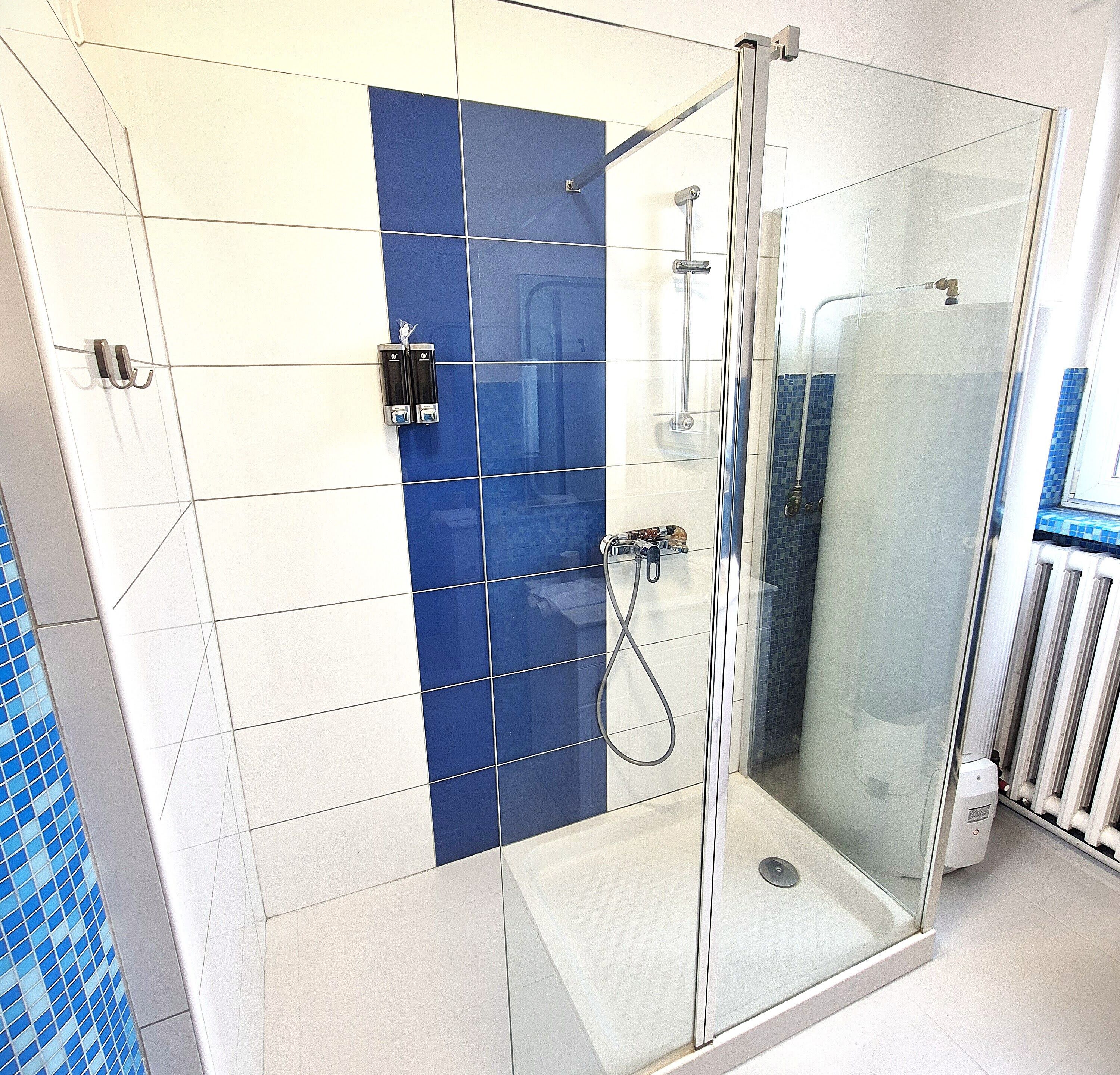 A shower area with a glass door, a blue and white tiled wall, and a hand dryer.