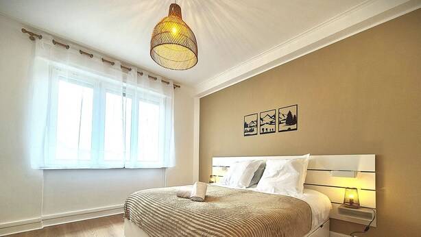 A bedroom with a bed, a window with curtains, a wall-mounted lamp, and a ceiling light fixture. - Rock in Share - Strozzi Suites - Brand-New Luxury 4-Bedroom Apartment with (Thionville)