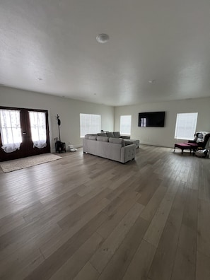 Ein geräumiges Wohnzimmer mit einer großen Couch, einem flachbildfernseher an der Wand und Holzböden.